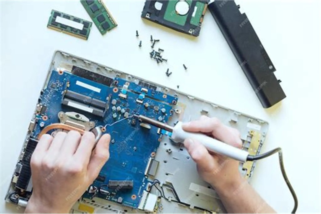 Technician working on a laptop motherboard using repair tools