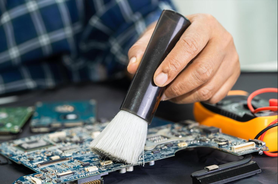 Technician cleaning dust from a laptop motherboard during preventive maintenance